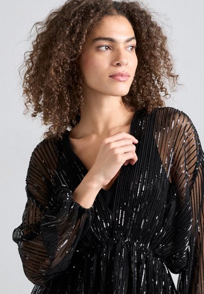 Robe noire en sequins avec manches plissées transparentes, décolleté en V et taille froncée. La texture scintillante et la coupe fluide rehaussent l'élégance.