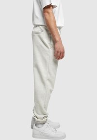 Ljust grå mjukisbyxor i avslappnad passform med sidofickor, ihop med vita sneakers. Materialet verkar mjukt med en slät textur.