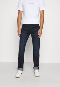 Mörkblå slim-fit denimjeans med fem fickor, lätt uppvikta fållar, i kombination med en enkel vit t-shirt och vita sneakers.