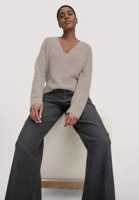 Beige gerippter Strickpullover mit V-Ausschnitt, kombiniert mit dunkelgrauen Schlagjeans. Der Pullover hat lange Ärmel und einen lockeren Schnitt.