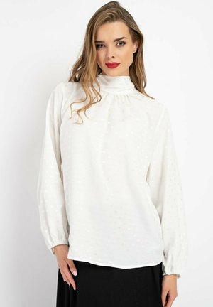 Weiße Bluse mit langen Ärmeln, hohem Halsauschnitt und gerafftem Detail. Mit gepunktetem Texturmuster und elastischen Bündchen. Leichtes Material.
