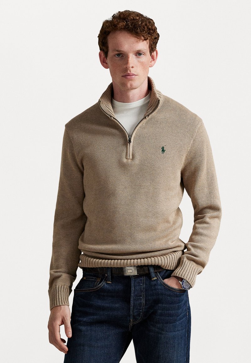 Beige zip-neck sweater lavet af struktureret strikstof, med ribbet talje, kontrastfarvet krave og lille grøn logo på brystet.