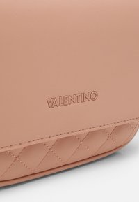 Pink leather handbag with quilted detailing at the bottom, featuring embossed "Valentino" logo on a smooth surface.