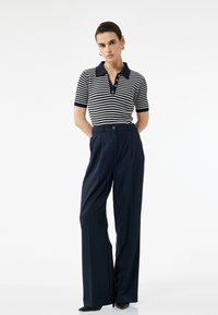 Camisa polo a rayas en blanco y negro con cuello y botones, combinada con pantalones de tiro alto en color marino que presentan un botón y pliegues.