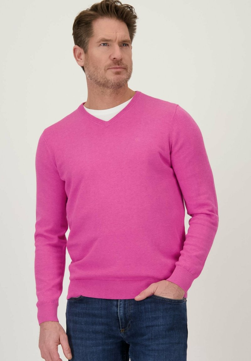 V-hals pullover in felroze gebreid stof met lange mouwen en geribbelde manchetten, gedragen over een wit shirt, gecombineerd met donkerblauwe jeans.