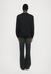 Črna trenirka z dolgimi rokavi, okroglo izrezana, z rebrastimi manšeti, v kombinaciji z razširjenimi temno sivimi kavbojkami in belimi teniskami. Zadnji pogled.