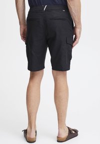 Sorte cargo-shorts med elastisk midjebånd og snor, to baklommer og sidelommer. Stoffet har en glatt tekstur og en subtil glans.