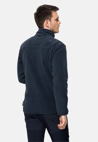 Donkerblauwe fleece jack met een hoge kraag, voorzien van een soepele textuur en een klein logo detail op de achterkant van de hals.