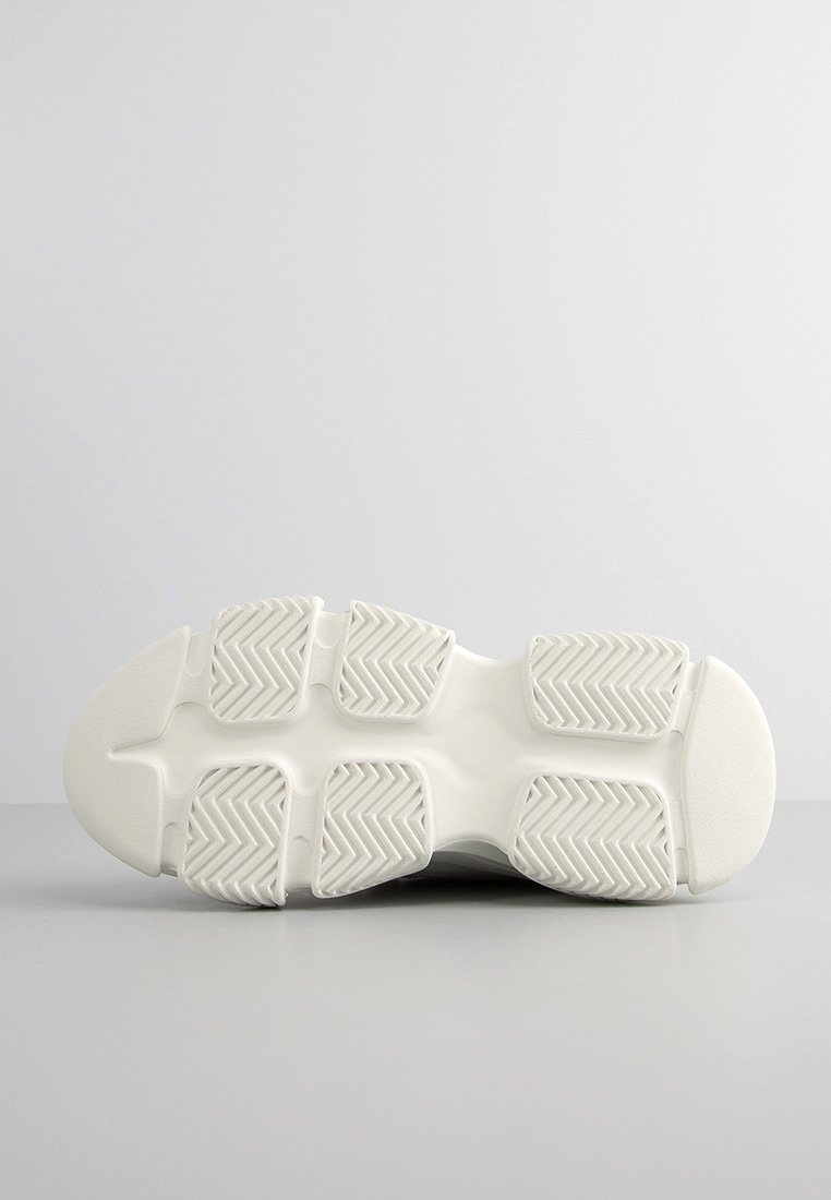 Suela de zapatilla blanca con patrón de agarre de goma texturizada. Presenta múltiples ranuras de tracción y una zona central suave. Punta redondeada para mayor estabilidad.