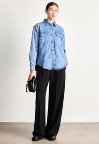 Ľanová svetlomodrá košeľa s zapínaním na gombíky, dvoma vreckami na hrudi a golierom. Kombinovaná s čiernymi širokými nohavicami a malou čiernou taškou.