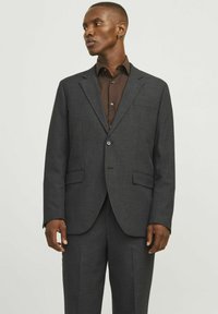 Dunkelgrau maßgeschneiderte Anzugjacke mit Revers, zwei Vorderaschen und Knopfverschluss, getragen über einem dunkelbraunen Hemd. Glatte Stoffoberfläche.