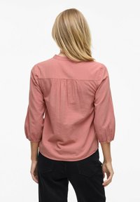 Rosafärgad, lätt blus med rund krage, rynkad detalj bak och trekvartslånga ärmar. Texturerad tyg med lätt lyster.