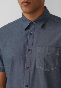 Korte mouwen shirt van donker denim met een knoopsluiting kraag, voorzien van een borstzak en zwarte knopen, aangevuld met witte stiksel details.