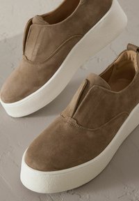 Baskets en daim marron avec un design à enfiler, des côtés élastiques et une semelle plateforme blanche épaisse. Texture lisse et lignes épurées.