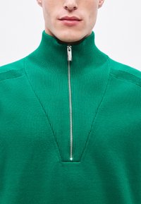 Zielony sweter dziany z wysokim kołnierzem, z zamkiem na ćwiartkę i prążkowaną fakturą. Dekolt w kształcie litery V z gładkim wykończeniem.