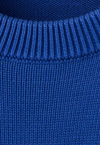 Gros plan sur l'encolure d'un pull en laine bleu montrant un col côtelé et un motif tricoté texturé.