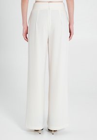 Pantaloni bianchi a gamba larga in tessuto liscio, con vita alta e chiusura con zip sulla schiena, che offrono una silhouette su misura e fluida.