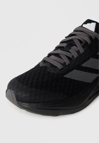 Czarny but sportowy z siateczkową cholewką, szarymi sznurowadłami i trzema odblaskowymi paskami. Podeszwa z teksturą i wzmocniony nosek.