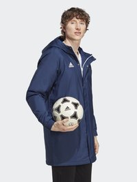 Námořnická vodotěsná bunda s kapucí, předním zipem a elastickými manžetami, kterou drží osoba se soccerovým míčem s černými akcenty.