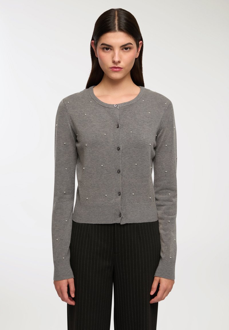 Cardigan lavorato a maglia grigio con scollo rotondo, chiusura frontale con bottoni e dettagli in perle sparse. Maniche lunghe e orlo a coste.