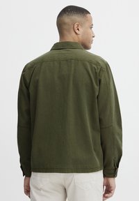 Olive green jacket with a relaxed fit, button cuffs, and a back yoke. Made of soft fabric with a textured finish.