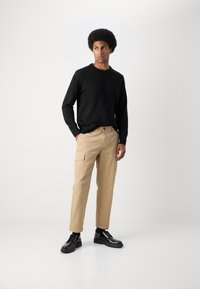 Black sweater, beige cargo pants with side pockets, and black lace-up shoes. Material appears lightweight with a smooth texture.