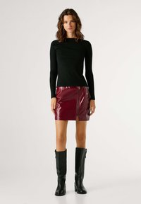 Μαύρη ριγέ μπλούζα με μακριά μανίκια, μίνι φούστα από γυαλιστερό δερμάτινο σε μπορντό με εμπρός φερμουάρ, και μαύρες δερμάτινες μπότες μέχρι το γόνατο.