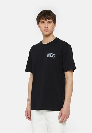 Camiseta de algodón negra con un pequeño logo azul en el lado izquierdo del pecho. Tiene un cuello redondo y mangas cortas, con un corte holgado.