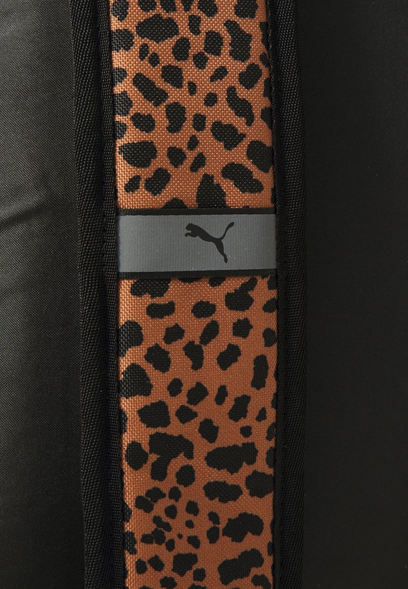 Tejido atlético negro con un panel de estampado de leopardo marrón y negro, y una franja horizontal gris que muestra el logo de Puma.