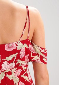 Rode bloemenprint off-shoulder top met korte mouwen, fijne bloemenpatronen in roze en groen, en dunne verstelbare bandjes.