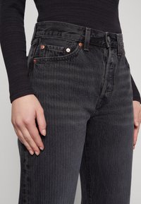 Černé džíny z denimu mají vysoký pas, decentní svislé pruhy, měděné nýty a klasický design s pěti kapsami. Texturovaná látka a jemný povrch.