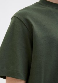 Olivenfarvet bomulds T-shirt med rund hals og korte ærmer; har en glat tekstur og pæne stikninger langs kanterne.
