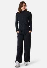 Svart dragkedja-jacka med lång ärm och ribbad textur, ihop med löst sittande svarta cargo-byxor med fickdetaljer.