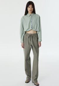 Camicetta verde chiaro a cropped con design a bottoni abbinata a pantaloni grigi chiari con cordino e vestibilità rilassata. Tessuto morbido e strutturato.