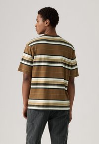 Camiseta de rayas marrón con líneas horizontales en crema, oliva y negro. Hecha de algodón, presenta un corte relajado y un diseño de cuello redondo.