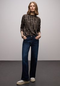 Szerokie ciemnoniebieskie jeansy zestawione z brązową koszulą w wzory z długim rękawem oraz jasnymi trampkami, charakteryzujące się luźnym krojem i podwiniętymi nogawkami.