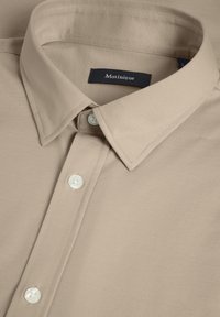 Beige Hemd mit Kragen aus strukturiertem Stoff, ausgestattet mit weißen Knöpfen und einem marineblauen Markenlabel, das im Kragen eingenäht ist.