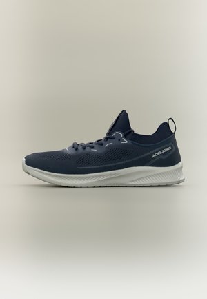 Basket athlétique tricotée bleu foncé avec semelle blanche, lacets et languette au talon, présentée de profil sur fond uni.