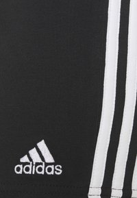 Pantalones cortos deportivos negros con tres rayas verticales blancas a lo largo de los lados y un logo bordado blanco cerca del dobladillo. Tela elástica.