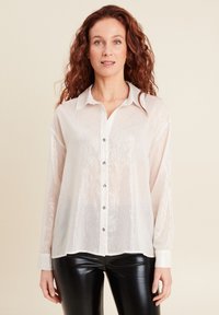 Camicia button-up beige chiaro con un lucido tessuto testurizzato, maniche lunghe e colletto a punta, con bottoni tono argento lungo il fronte.