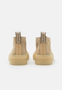 Paire de bottines beige en daim avec semelles crêpe et languettes en tissu portant l'étiquette GANT, vues de dos sur fond blanc.