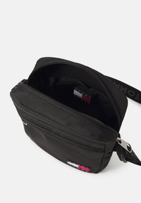 Melnas auduma plecu soma ar rāvējslēdzēja aizdari, iekļaujot iekšēju birku sarkanas, baltas un zilas krāsas. Gluda tekstūra, kompakta forma.