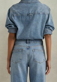Hele sinine denim särgiga, mille varrukad on üles rullitud, sisaldab õmblust ja riputusaasa. Kõrge vöökoht, hele sinine teksapüksid, millel on kaks tagumist taskut.