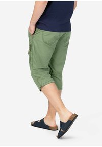 Grüne Cargo-Shorts aus strukturiertem Gewebe, mit seitlichen Taschen, umgeschlagenen Säumen und passendem Bund. Kombiniert mit dunklen Sandalen.
