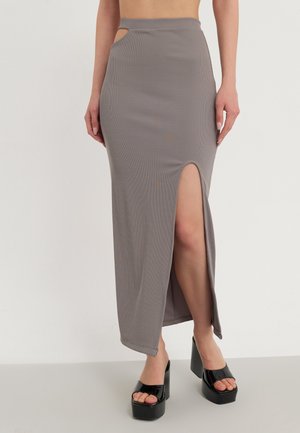 Femme portant une jupe longue grise taille haute avec une fente à la cuisse et une découpe à la taille, associée à des sandales à plateforme noires.