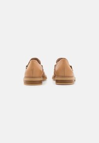 Tan leren schoenen met een gladde afwerking, met een lage hak en zichtbare stiksels langs de randen. De achterkant toont een ronde vorm.