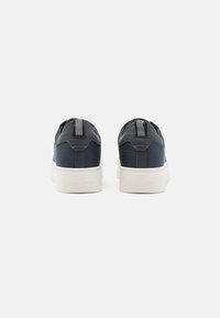 Navy sneakers featuring a smooth leather upper with a textured back, white rubber sole, and striped pull tab at the heel.