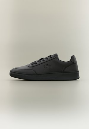 Sort lavt snøresneaker med snøredesign og præget krokodille-logo på siden, vist fra det ydre sideprofil.