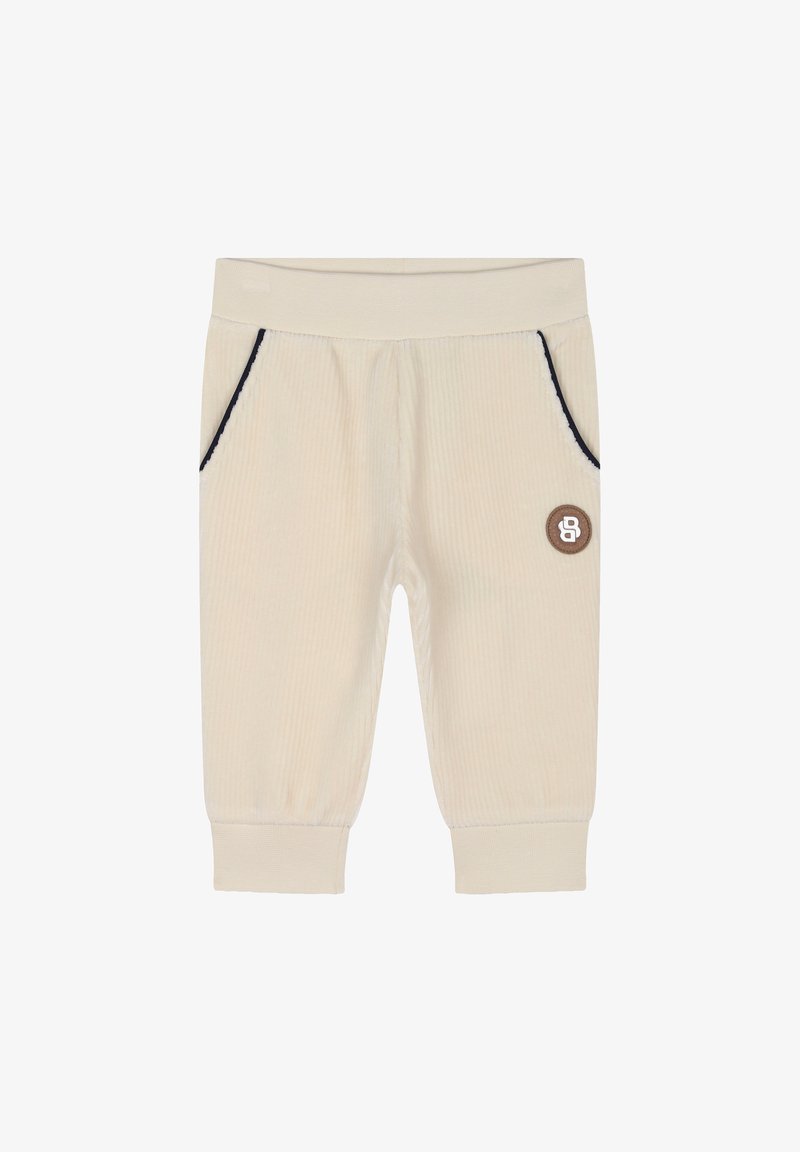 Jogging en velours côtelé beige clair avec des coutures bleu marine, deux poches latérales et un petit patch logo marron à l'avant. Texture douce, taille élastique.