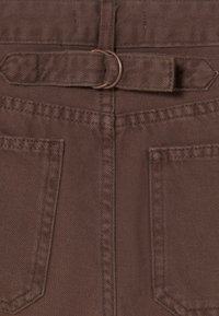 Primer plano de pantalones de tela marrón con dos bolsillos traseros y una correa ajustable con hebilla de anillo en D de metal en la cintura.